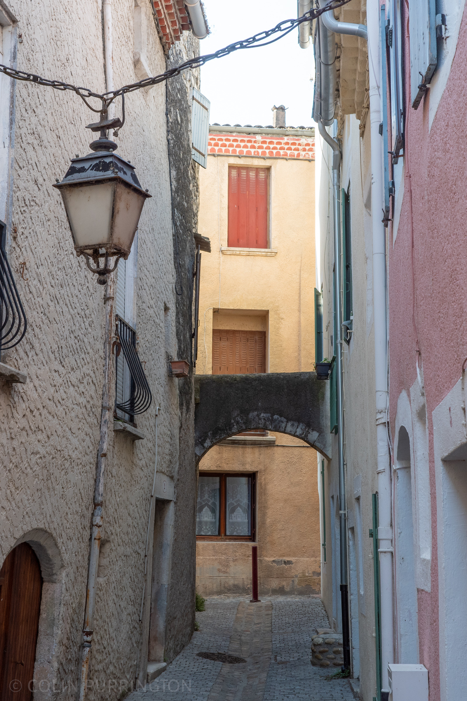 Arched stone and plaster structure between two buildings on a very, very narrow cobblestone street.