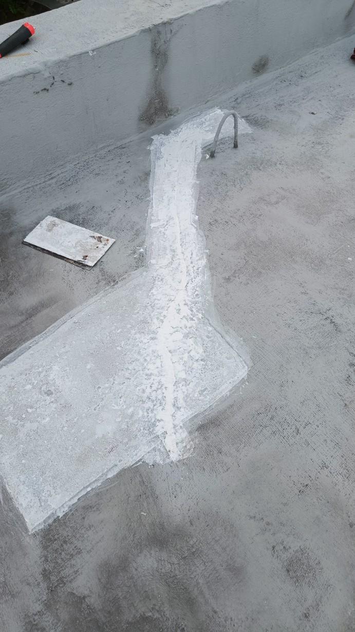 Photo of the same crack, in more or less the same orientation, but now filled in with the crack sealant (polymer-modified cement). The crack itself is filled tightly, but only after a primer coat of the same stuff mixed 1:1 with water is painted into the crack and onto the surrounding area of the slab.